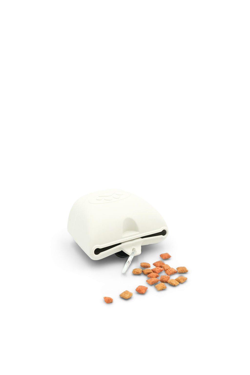 A white countertop food chopper or shredder with a small pile of shredded orange food pieces spilling out from the front, photographed on a clean white background.