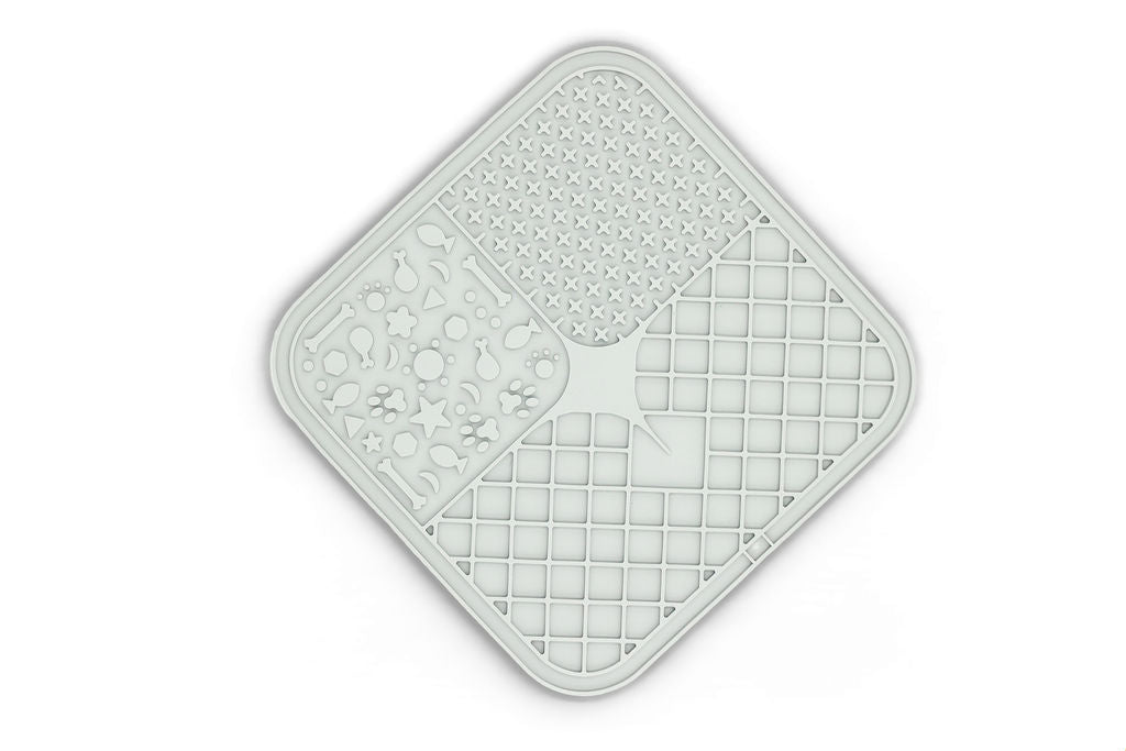 A square, diamond-shaped silicone mat with rounded corners, featuring four distinct textured quadrants: a honeycomb pattern, a moon and star motif, a grid pattern, and a central arrow design. The mat is light gray with a subtle drop shadow on a white background.