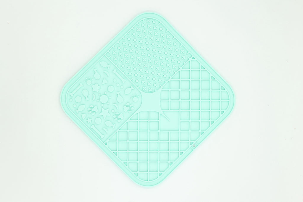A mint green silicone kitchen mat with a diamond-shaped design, featuring three distinct textured sections: a circular pattern, a central star with a wavy center, and a grid pattern, shown on a plain white background.