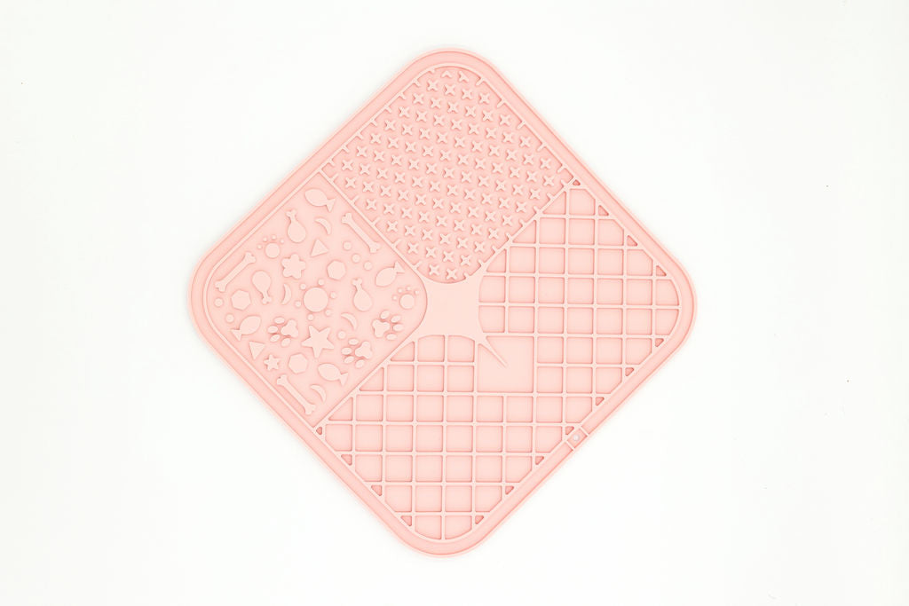A light pink silicone kitchen mat with a diamond-shaped design, featuring three textured sections: a floral pattern on the left, a dotted grid on the top right, and a grid pattern on the bottom right, shown on a plain white background.
